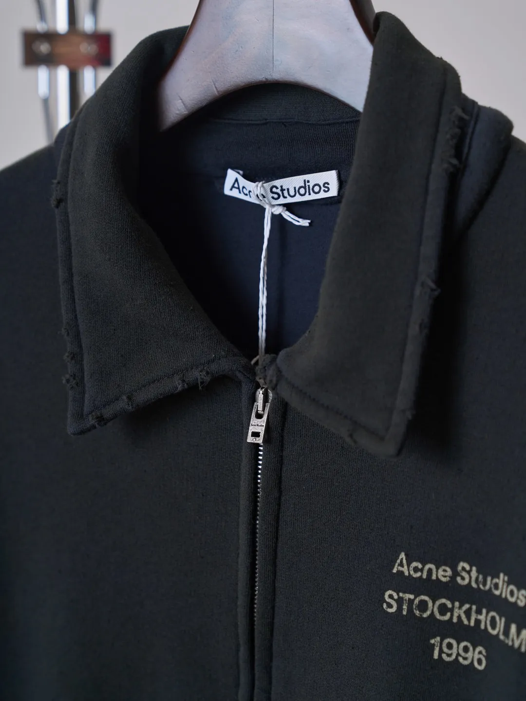 [Real auction] Acne Studios Retro distressed letter print zipper jacket [In Stock] Logo stamp at front, side-seam pockets, and ribbed cuffs and hem. Regular fit, just above the waist. It adopts a 3-strand composite fleece structure with 32 counts for the top layer and 40 counts for the bottom layer, with a weight of g/㎡. The 32-count yarn on the top layer is fine and smooth, giving the surface a smooth touch and excellent anti-pilling properties; the 40-count 3-ply yarn on the bottom layer is treated with a raising process to form a rich and soft fluff layer, providing excellent warmth and skin-friendly wrapping. With 21 2×2 ribs, the g/㎡ weight ensures that the collar, cuffs and hem have excellent tensile fatigue resistance and shape retention capabilities. During piece dyeing, the entire fabric is immersed in the dye vat after weaving, and the dye molecules fully penetrate into the fibers, ensuring full, deep colors and excellent color fastness. Each batch of dyeing produces subtle differences, making the color tone of the single product unique. On this basis, the paint is sprayed irregularly on the surface of the garment through manual spray painting to create a splash-like retro effect. The distressed processing of holes causes the color to fade and mottle in parts. The ribbed trim is also treated to form slight whitening and fluffing, which visually echoes the spray-painted effect on the body, making the new clothes appear as if they have been worn for a long time and exposed to the sun. The front logo stamp uses a slurry printing process. The printing slurry contains a special microcapsule foaming agent. After being baked at high temperature, the slurry layer expands to form three-dimensional bulges, and the surface presents a granular texture similar to inkjet paint. This process simulates the effect of random drops of pigment after being atomized during spray gun spraying. The edges of the pattern present a natural feathering transition, rather than the rigid boundaries of glue printing. The printing surface has a fine graininess and soft elasticity to the touch, forming a closed loop of the process with the distressed effect of the spray painting on the body.